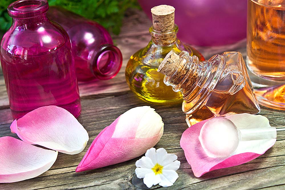 Blüten und Öle Flaschen mit Massageölen und Rosenblüten auf einem Holztisch für Aromatherapie.