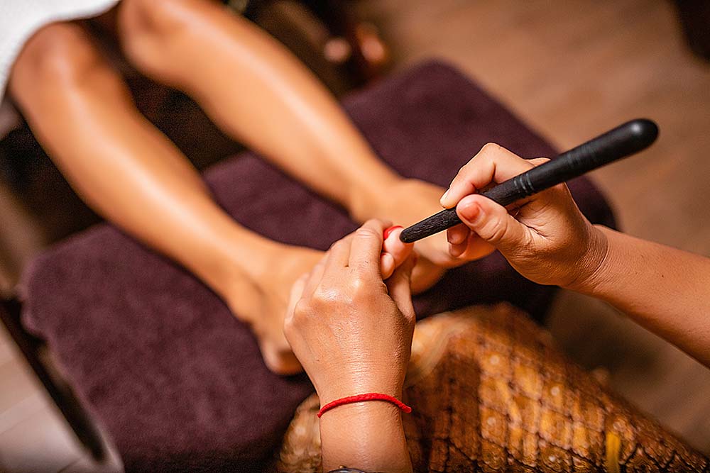 Fußmassage Person erhält eine Fußmassage mit einem Holzstab an der großen Zehe.